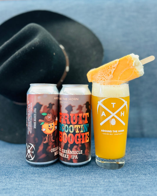 Two cans of 'Fruit Scootin' Boogie' beer and a glass with an orange creamsicle beer and a popsicle on a denim surface.