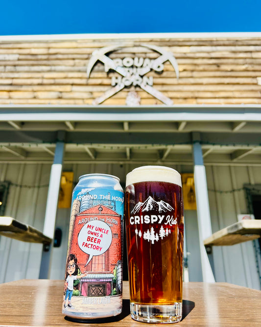Crispy Kid beer can and glass on a table with a brewery in the background