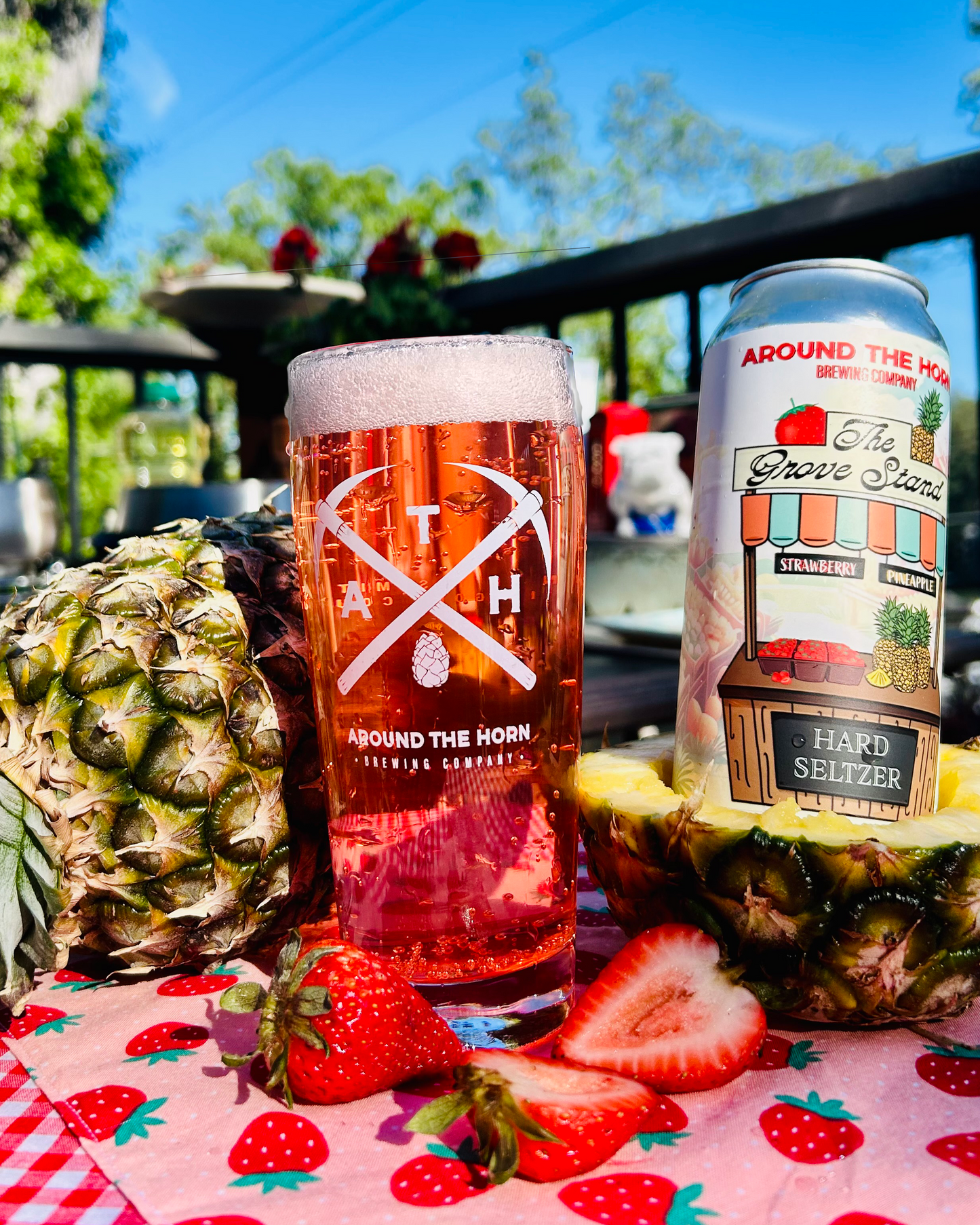 Glass of pink hard seltzer with pineapple and strawberries on a checkered tablecloth.