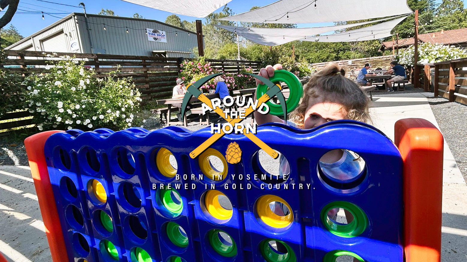 A little girl playing a giant Connect 4 game outdoors in The Corral beer garden with the Around The Horn logo imposed on top of the image.