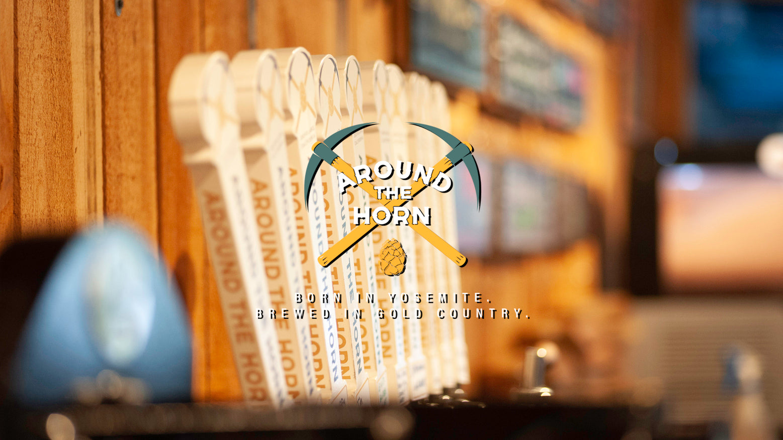 White beer tap handles against a wood wall with Around The Horn's logo superimposed on top of the image. 